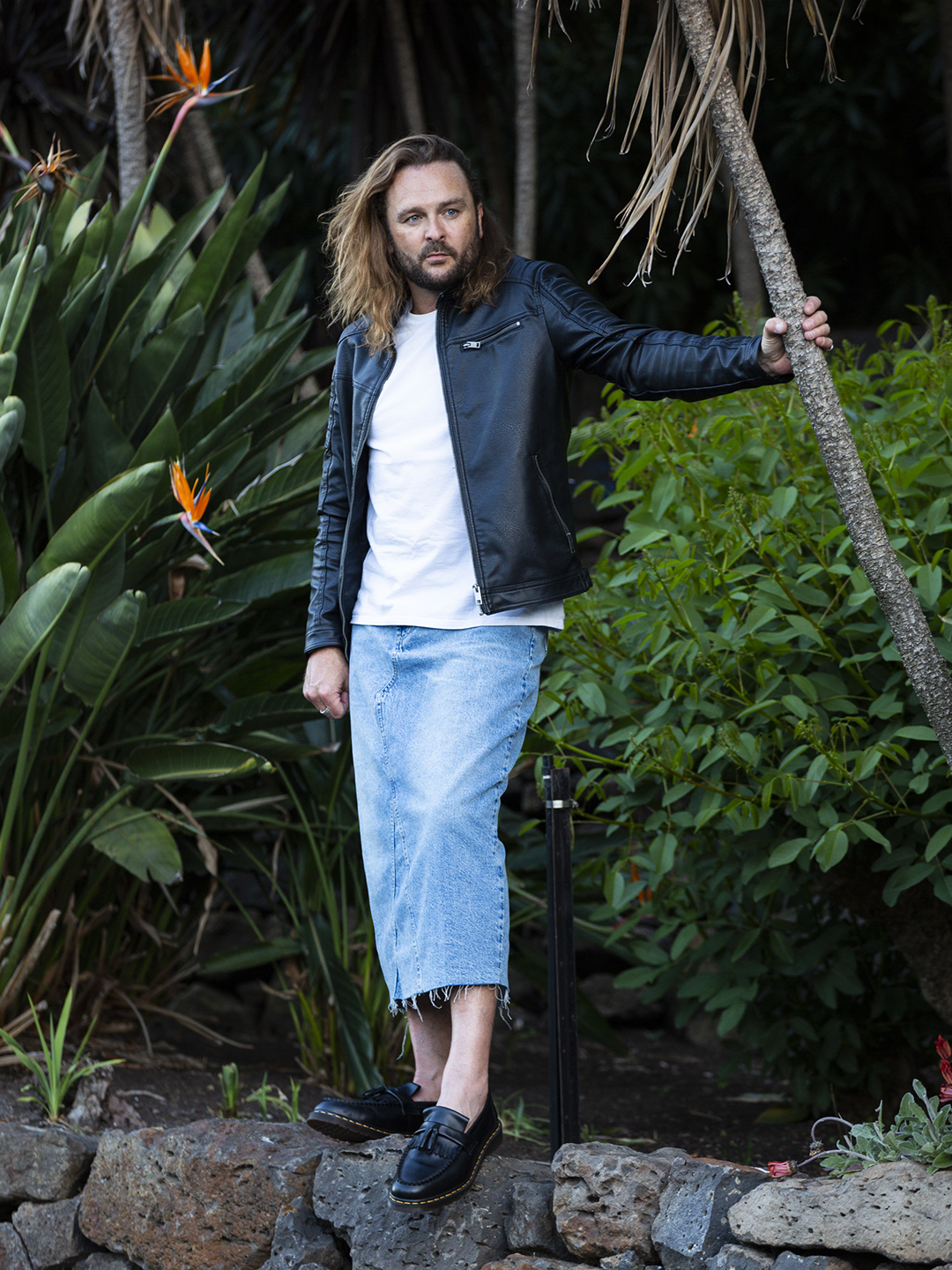 Brad in a leather jacket and long denim skirt in a garden