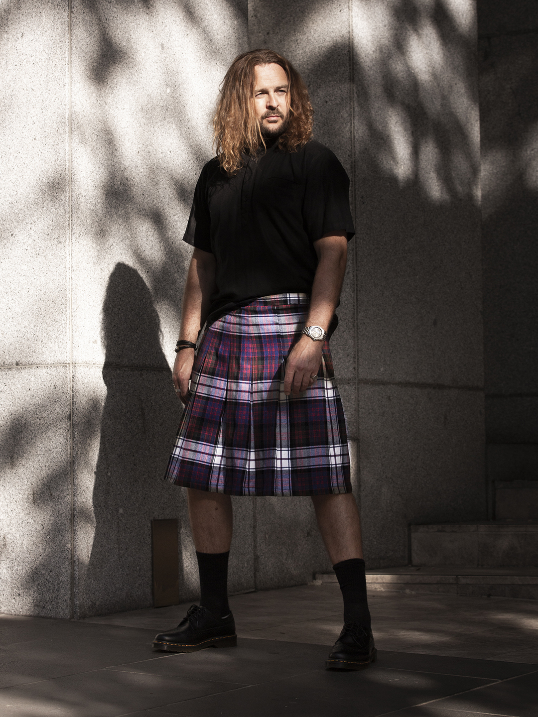 Brad wearing a red and navy pleated kilt with a black shirt and boots